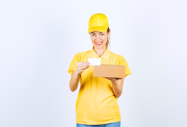 Corriere femminile in uniforme gialla che consegna un pacco e offre il suo biglietto da visita.