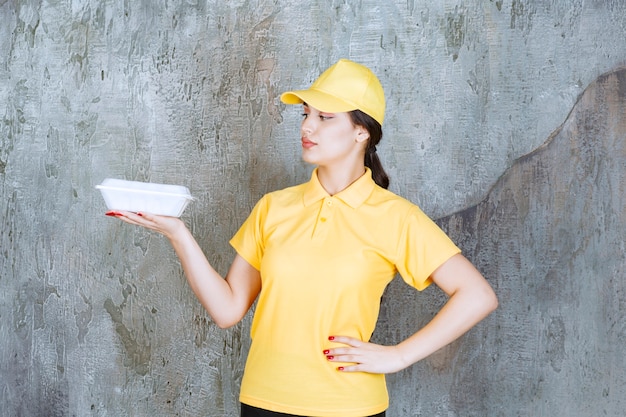 Corriere femminile in uniforme gialla che consegna una scatola bianca da asporto