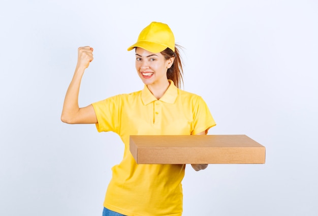 Corriere femminile in uniforme gialla che tiene un pacco di cartone e mostra il pugno.