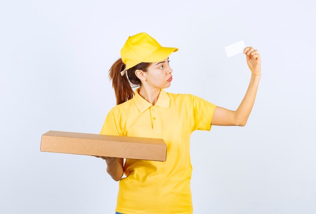 Corriere femminile in uniforme gialla che tiene un pacco di cartone e presenta il suo biglietto da visita.