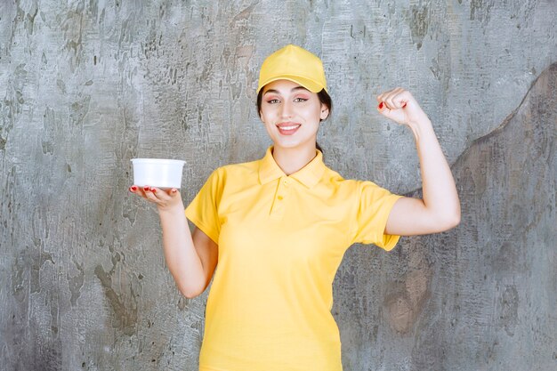 Corriere femminile in uniforme gialla che tiene una tazza da asporto e si gode il prodotto