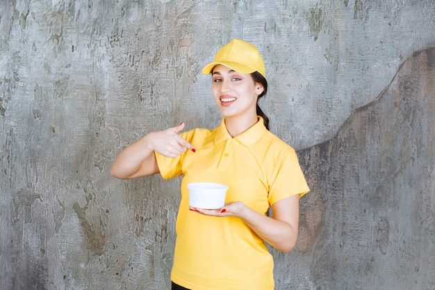 Corriere femminile in uniforme gialla che tiene una tazza da asporto