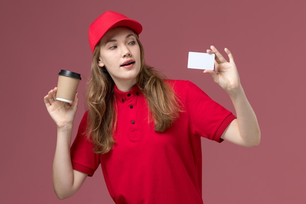 corriere femminile in uniforme rossa che tiene caffè bianco della carta sulla consegna dei lavoratori di servizio di colore rosa chiaro, uniforme di lavoro