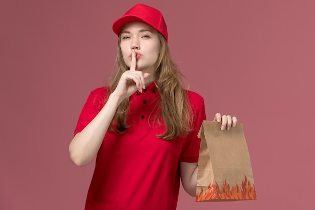 corriere femminile in uniforme rossa che tiene il pacchetto di cibo di carta sul rosa chiaro, consegna del servizio di lavoro in uniforme