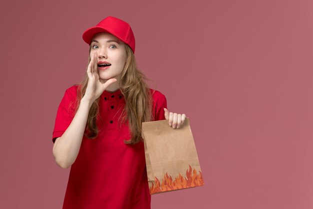 corriere femminile in uniforme rossa che tiene il pacchetto di cibo e sussurra sulla consegna dei lavoratori di servizio di colore rosa chiaro, uniforme di lavoro
