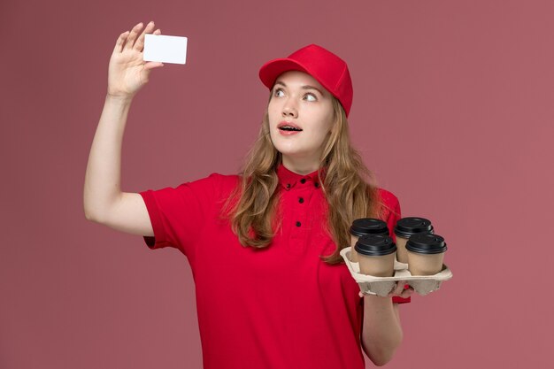 corriere femminile in uniforme rossa che tiene le tazze di caffè con la carta sul rosa, consegna del servizio uniforme