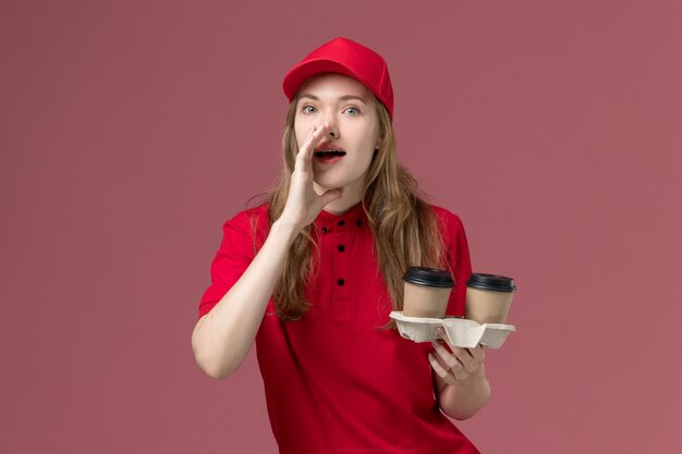 corriere femminile in uniforme rossa che tiene le tazze di caffè e bisbiglia sul rosa, lavoratore di lavoro di consegna del servizio uniforme
