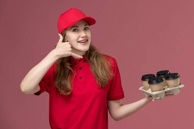 corriere femminile in uniforme rossa che tiene le tazze di caffè sorridente in posa sul lavoratore di lavoro di consegna servizio rosa, uniforme