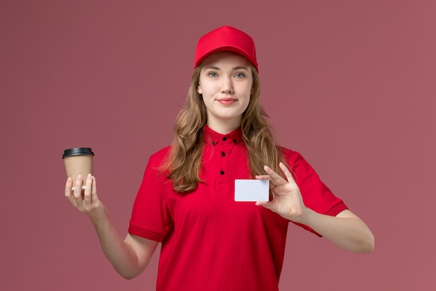 corriere femminile in uniforme rossa che tiene tazza di caffè e carta sulla consegna del lavoratore di servizio di colore rosa chiaro, uniforme di lavoro