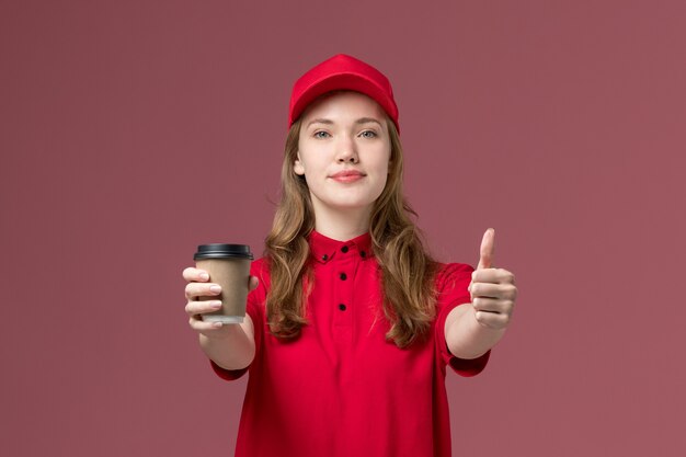 corriere femminile in uniforme rossa che tiene tazza di caffè in posa su rosa chiaro, consegna lavoratore servizio uniforme di lavoro