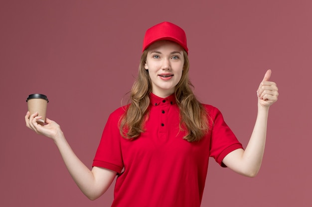 corriere femminile in uniforme rossa che tiene tazza di caffè su rosa chiaro, consegna del servizio lavoratore uniforme di lavoro