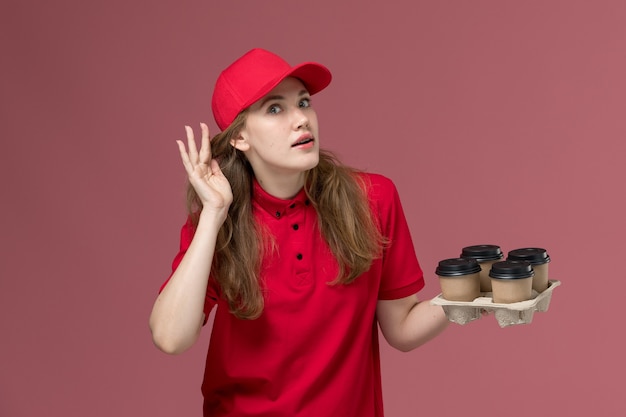 corriere femminile in uniforme rossa che tiene tazze di caffè cercando di ascoltare il lavoratore di lavoro di consegna servizio rosa, uniforme