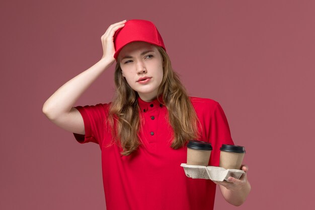 corriere femminile in uniforme rossa che tiene tazze di caffè e pensa al lavoro di consegna del servizio rosa, uniforme