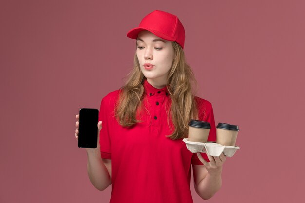 corriere femminile in uniforme rossa che tiene tazze di caffè e telefono sul lavoro di operaio consegna servizio rosa, uniforme
