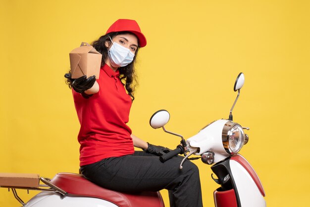 Corriere femminile vista frontale in maschera con piccolo pacchetto di cibo su sfondo giallo servizio pandemia lavoratore uniforme covid consegna lavoro