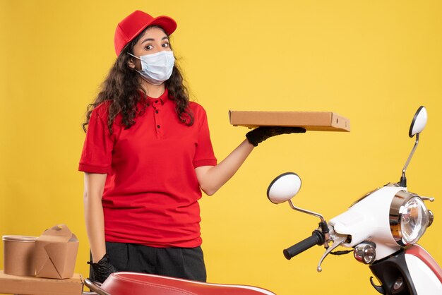 Corriere femminile vista frontale in uniforme rossa con scatola della pizza sullo sfondo giallo lavoratore di servizio covid- virus pandemico consegna del lavoro