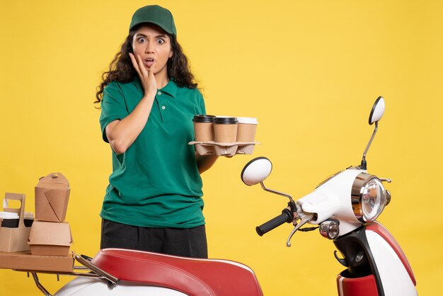 Corriere femminile vista frontale in uniforme verde con caffè su sfondo giallo lavoratore servizio consegna lavoro lavoro cibo donna