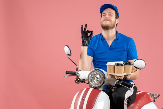 Corriere maschio di vista frontale che si siede sulla bici e che tiene le tazze di caffè sul rosa