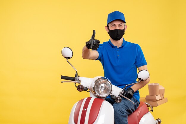 Corriere maschio di vista frontale che si siede sulla bici nella mascherina sulla pandemia di lavoro di covid di consegna del servizio di lavoro giallo