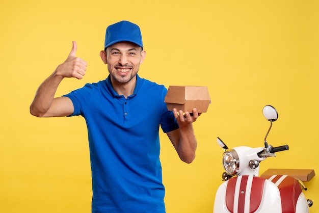 Corriere maschio di vista frontale che tiene piccolo pacchetto di cibo sul lavoratore giallo della bici di colori di lavoro di servizio di consegna del lavoro del lavoro