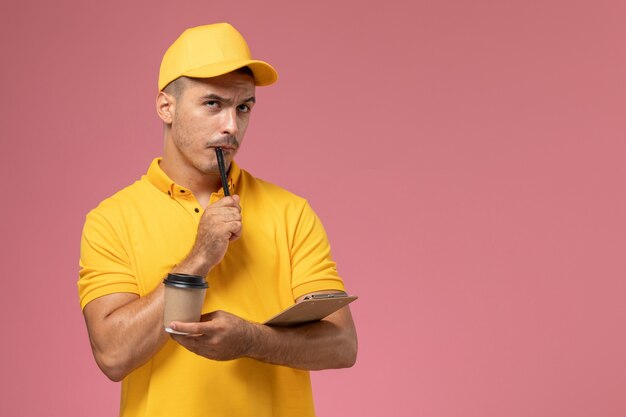 Corriere maschio di vista frontale in note di scrittura della tazza di caffè di consegna della tenuta uniforme gialla su fondo rosa