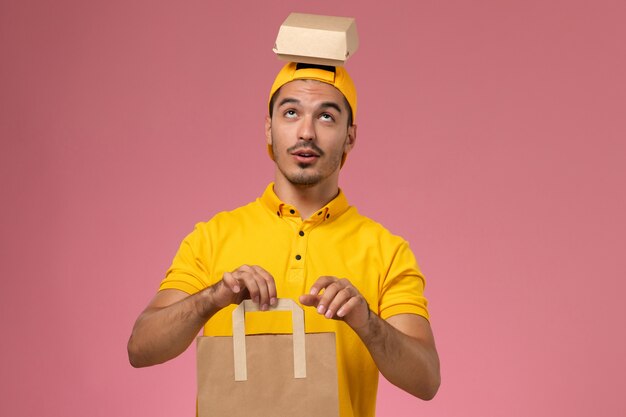 Corriere maschio di vista frontale in pacchi di cibo di consegna uniforme giallo della tenuta su fondo rosa