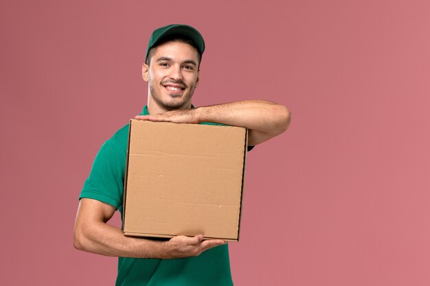 Corriere maschio di vista frontale in scatola di cibo della tenuta uniforme verde con il sorriso sui precedenti rosa