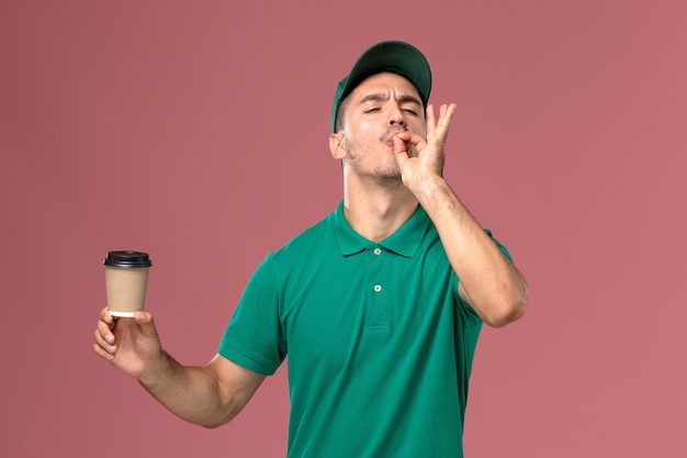 Corriere maschio di vista frontale in tazza di caffè di consegna uniforme della tenuta verde sullo scrittorio rosa