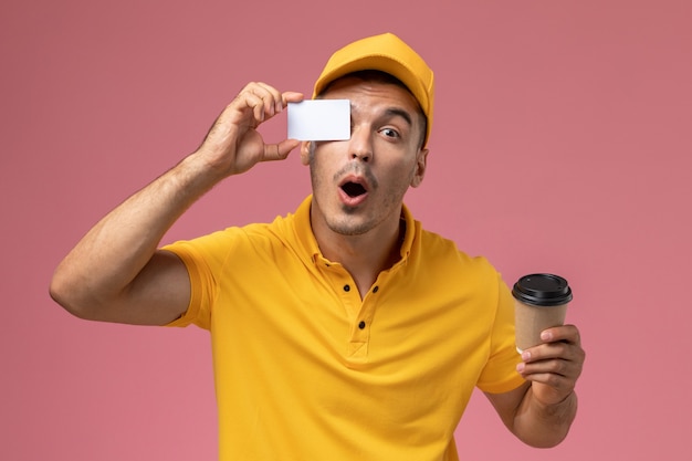 Corriere maschio di vista frontale in tazza di caffè e carta di consegna della tenuta uniforme gialla sullo scrittorio rosa