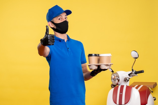 Corriere maschio di vista frontale in uniforme blu che tiene caffè sul servizio di lavoro di colore giallo covid - consegna del lavoro uniforme pandemica