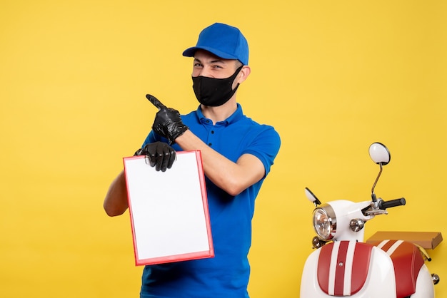 Corriere maschio di vista frontale in uniforme blu che tiene la nota del file sul lavoro di colore giallo pandemia servizio covid-consegna uniforme