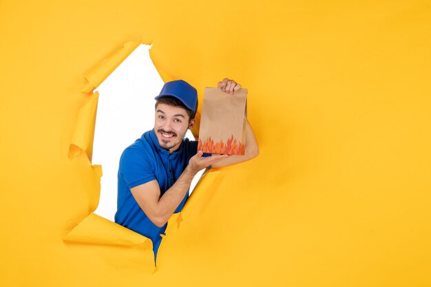 Corriere maschio di vista frontale in uniforme blu che tiene pacchetto di cibo su spazio giallo