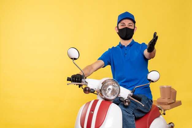Corriere maschio di vista frontale in uniforme blu e maschera su un lavoro di servizio di bici pandemico di consegna covid virus di lavoro giallo