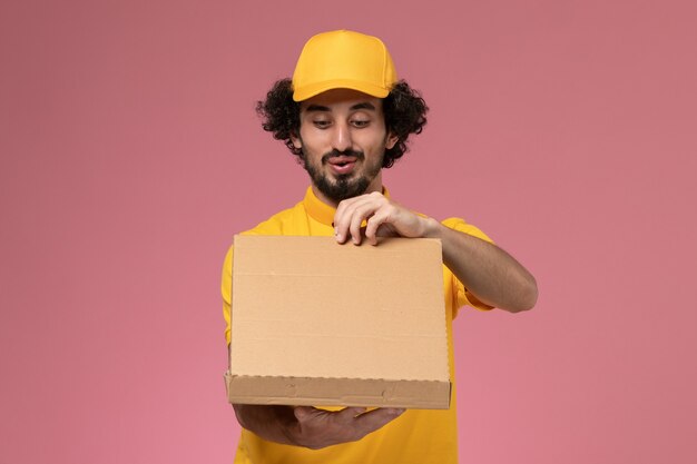 Corriere maschio di vista frontale in uniforme gialla che tiene la scatola di consegna del cibo sul muro rosa chiaro