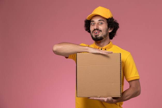 Corriere maschio di vista frontale in uniforme gialla che tiene la scatola di consegna del cibo sul muro rosa chiaro