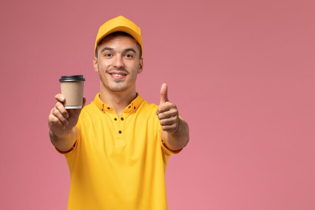 Corriere maschio di vista frontale in uniforme gialla che tiene tazza di consegna del caffè con il sorriso sui precedenti rosa