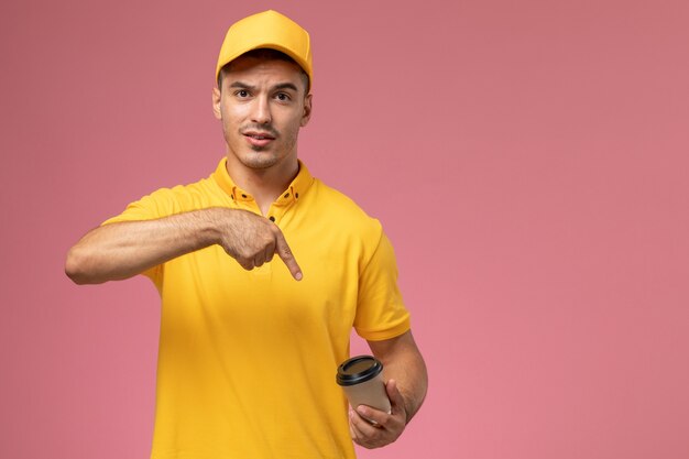 Corriere maschio di vista frontale in uniforme gialla che tiene tazza di consegna del caffè marrone sui precedenti rosa