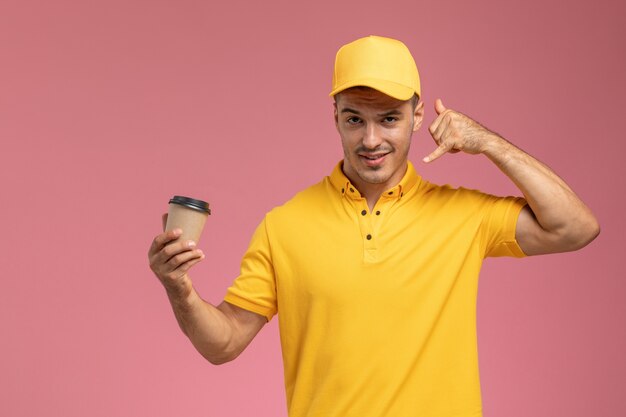 Corriere maschio di vista frontale in uniforme gialla che tiene tazza di consegna del caffè marrone sui precedenti rosa