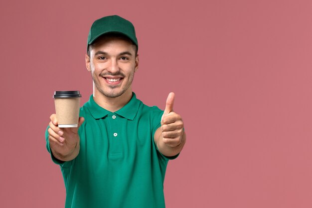 Corriere maschio di vista frontale in uniforme verde che tiene la tazza di caffè di consegna con il sorriso sui precedenti rosa