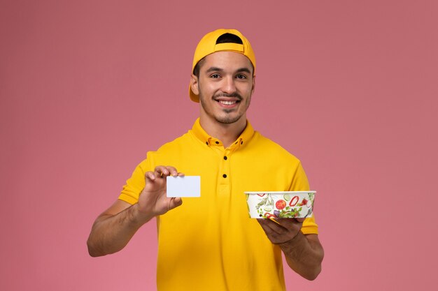 Corriere maschio di vista frontale nella ciotola di consegna della tenuta della tenuta uniforme gialla con la carta sui precedenti rosa.