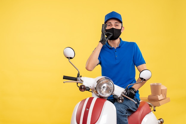 Corriere maschio di vista frontale sulla bici in maschera su una consegna pandemic di lavoro covid-uniforme di servizio di lavoro giallo