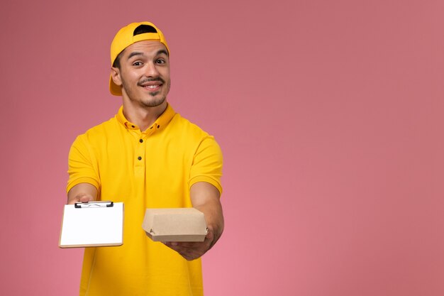 Corriere maschio di vista ravvicinata anteriore in blocco note giallo della tenuta uniforme e piccolo pacchetto di cibo sulla parete rosa