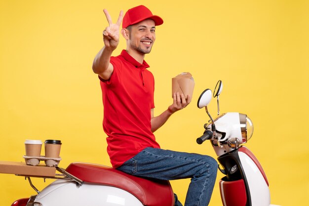 Corriere maschio giovane di vista frontale in cibo di consegna uniforme rosso della tenuta su fondo giallo