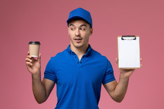 corriere maschio in uniforme blu che tiene il blocco note della tazza di caffè sul rosa, consegna del servizio uniforme del lavoratore