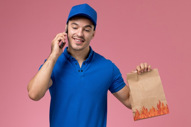 corriere maschio in uniforme blu che tiene il pacchetto di cibo di consegna parlando al telefono in rosa, consegna uniforme del servizio di lavoro