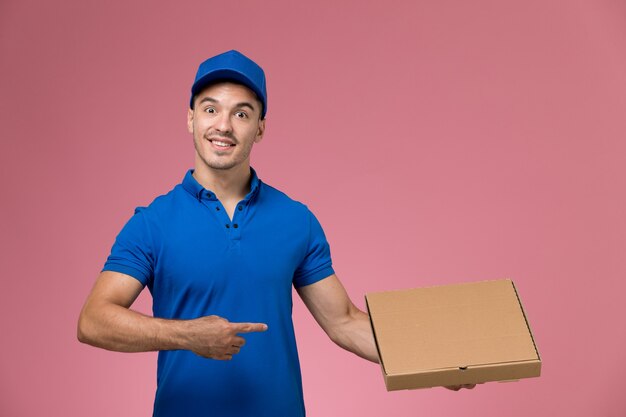 corriere maschio in uniforme blu che tiene la scatola di consegna di cibo e sorridente sul rosa, consegna del servizio uniforme di lavoro lavoratore