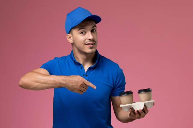 corriere maschio in uniforme blu che tiene le tazze di caffè di consegna che posano sulla consegna rosa, uniforme del servizio del lavoratore di lavoro