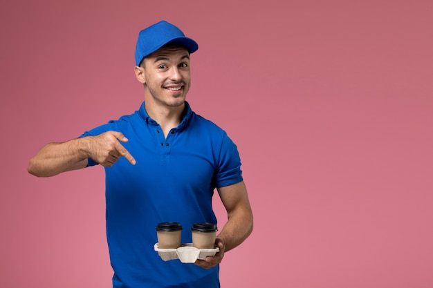 corriere maschio in uniforme blu che tiene le tazze di caffè di consegna con il sorriso sulla consegna rosa, uniforme del servizio del lavoratore di lavoro