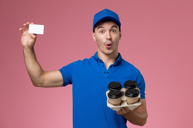 corriere maschio in uniforme blu che tiene le tazze di caffè di consegna e carta sulla consegna rosa, uniforme del servizio del lavoratore di lavoro