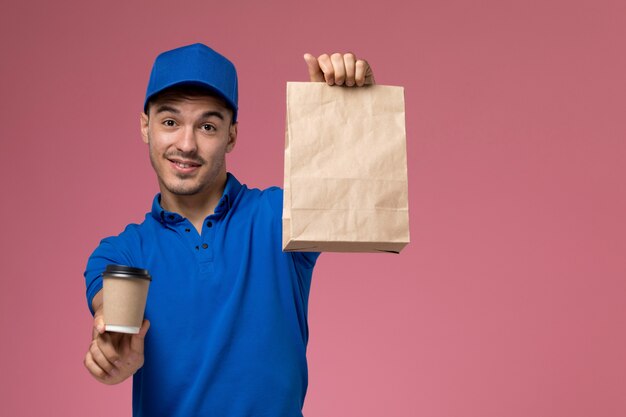 corriere maschio in uniforme blu che tiene le tazze di caffè di consegna e che sorride sulla consegna rosa, uniforme del servizio del lavoratore di lavoro